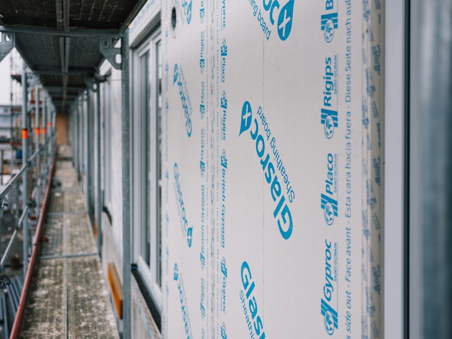 Eine Nahaufnahme eines im Bau befindlichen Gebäudes zeigt Glasroc-Schalungsplatten an der Außenwand, umgeben von Gerüsten und Metallstegen.