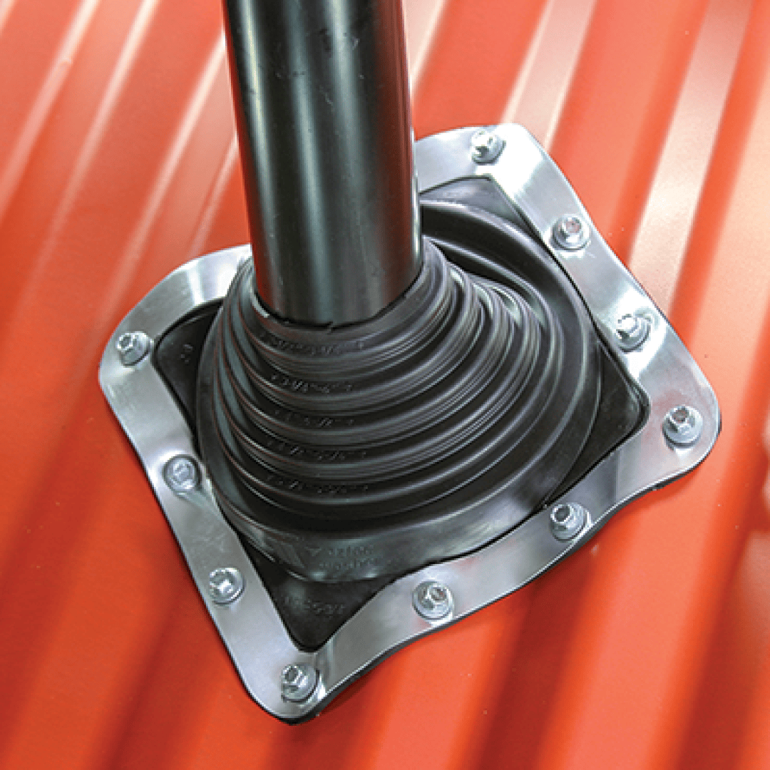 A close-up of a black rubber hose sleeve that seals a pipe penetration on a red corrugated sheet metal roof and is fastened with screws around a metal flange.