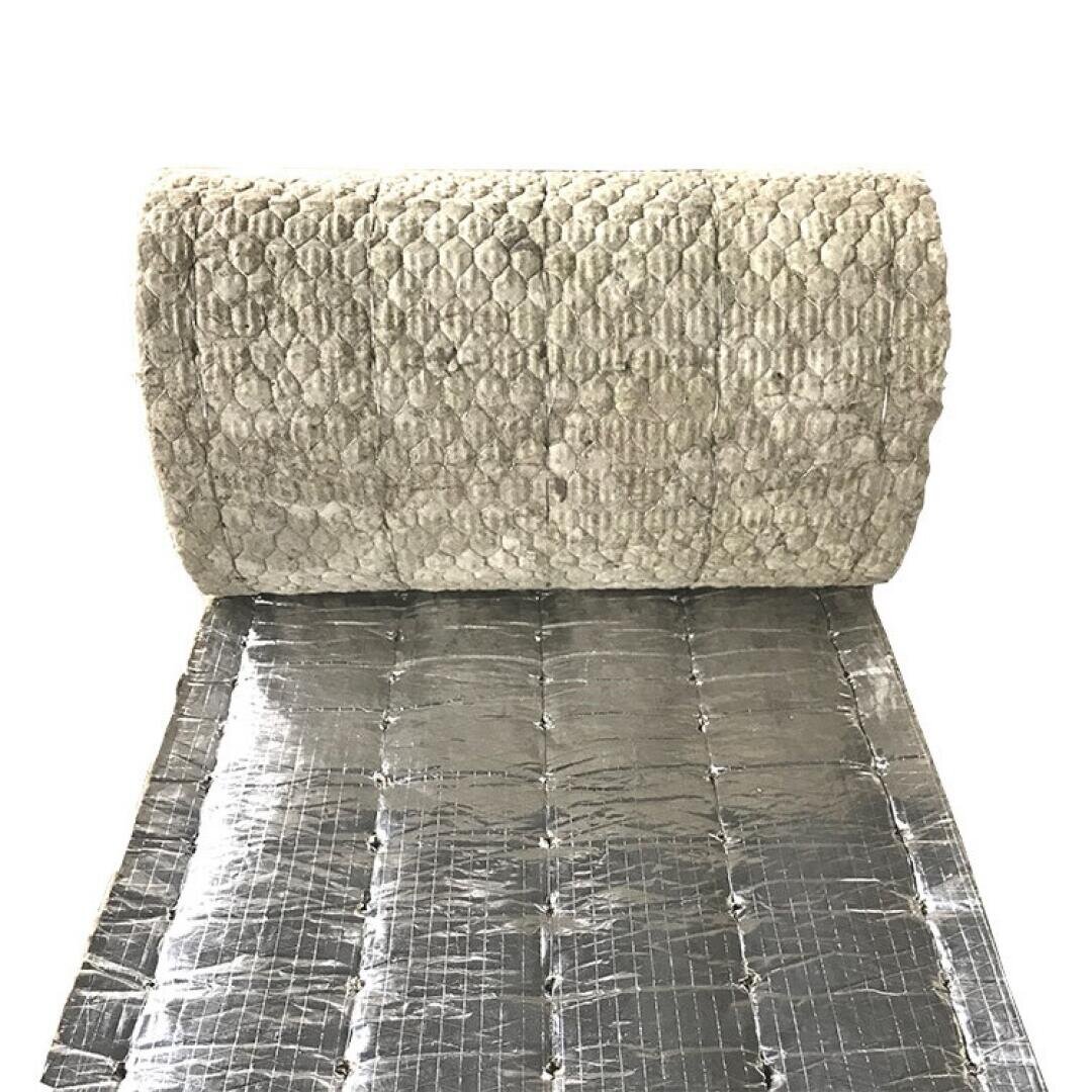 A roll of insulation material with a textured, light-colored fibrous surface on top and a shiny, reflective foil layer on the bottom, partially unrolled on a flat surface.
