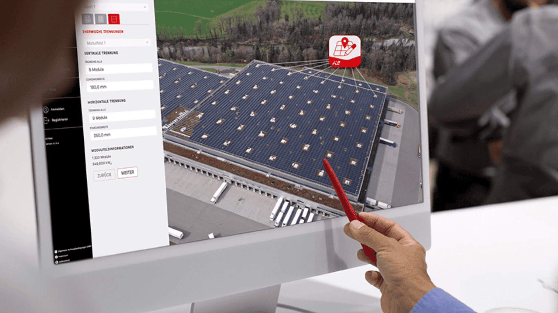 A person points at a computer screen displaying an aerial view of a large building with solar panels on its roof, while a software interface with settings is visible on the left side of the monitor.
