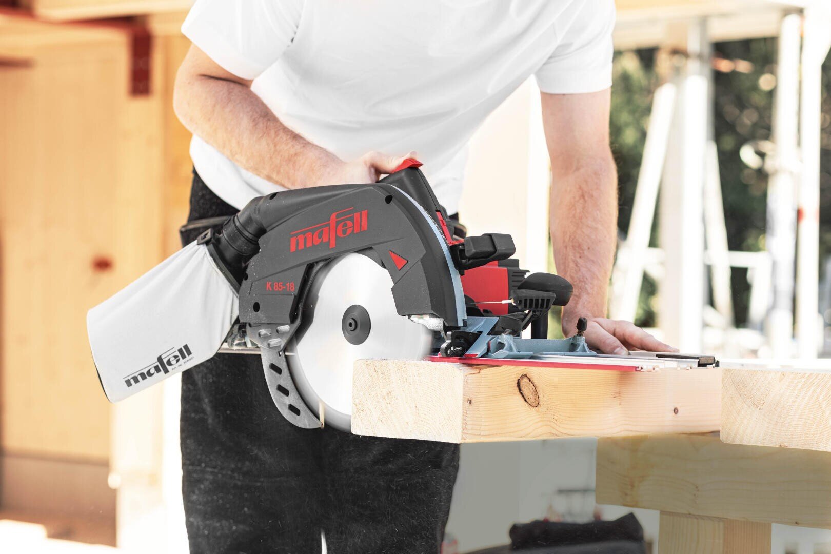 Eine Person mit weißem Hemd schneidet mit einer Mafell-Kreissäge ein Holzbrett auf einer Werkbank in einem hellen Innenraum für Holzarbeiten.