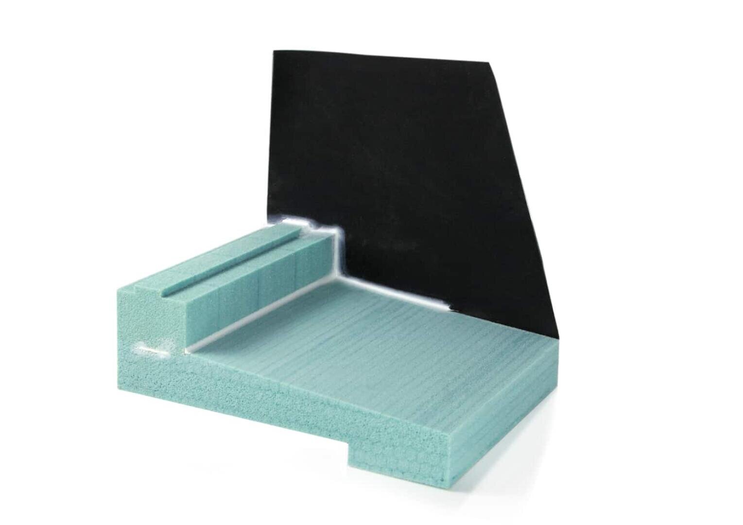 Ein Abschnitt einer hellblauen Hartschaumisolierung mit einer vertikalen schwarzen Barriere auf weißem Hintergrund. Der Schaumstoff ist so geschnitten, dass seine geschichtete Struktur und die vertieften Rillen sichtbar werden.