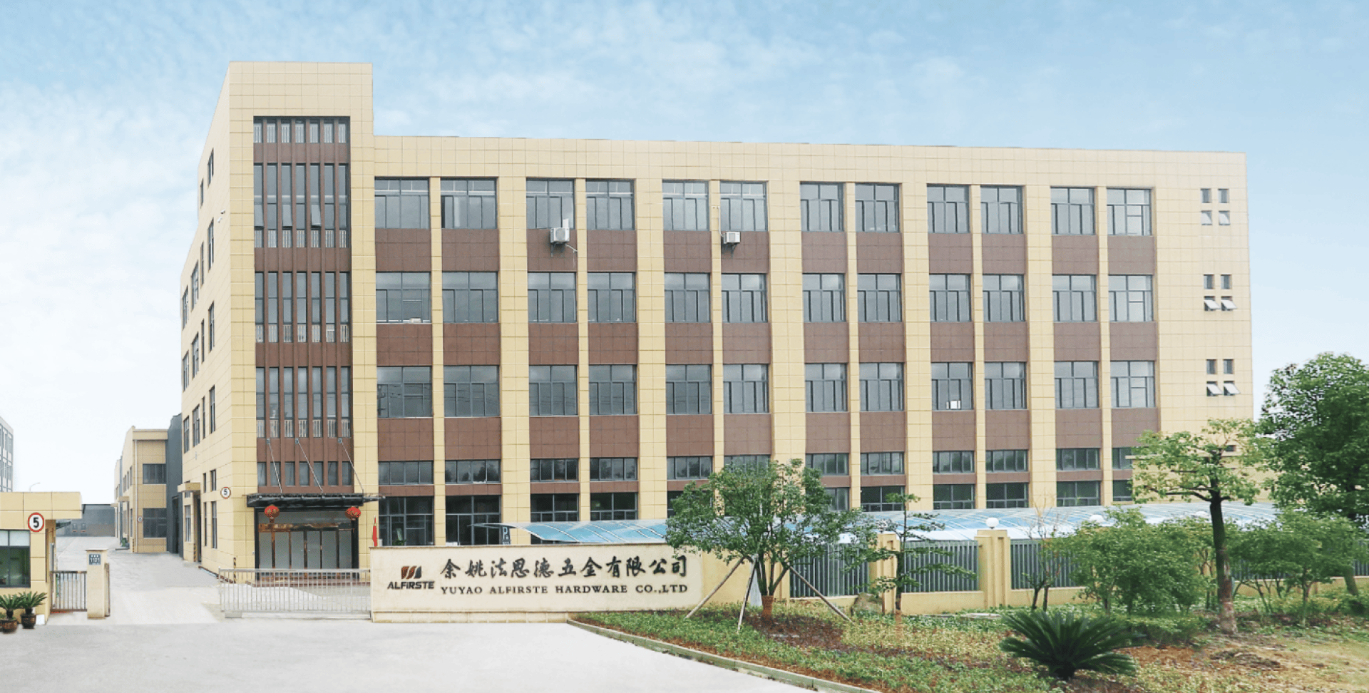 Ein modernes, vierstöckiges Industriegebäude mit großen Fenstern und einer beige-braunen Fassade. Ein Schild mit chinesischen Schriftzeichen und einem Firmennamen steht am Eingangstor, in der Nähe gibt es Grünflächen und Bäume.