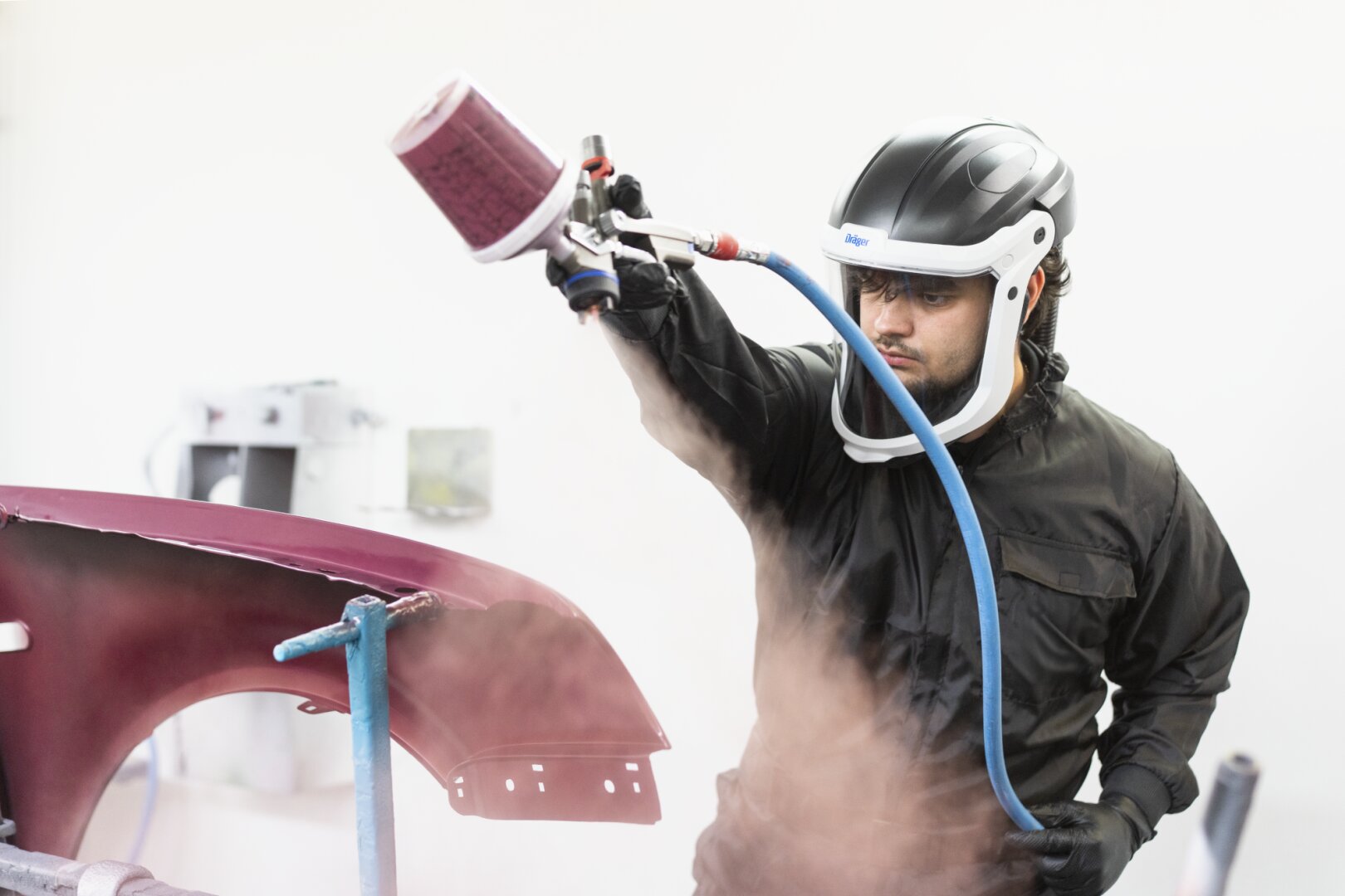 Ein Mann, der einen Helm trägt und eine Spritzpistole über ein Auto hält.