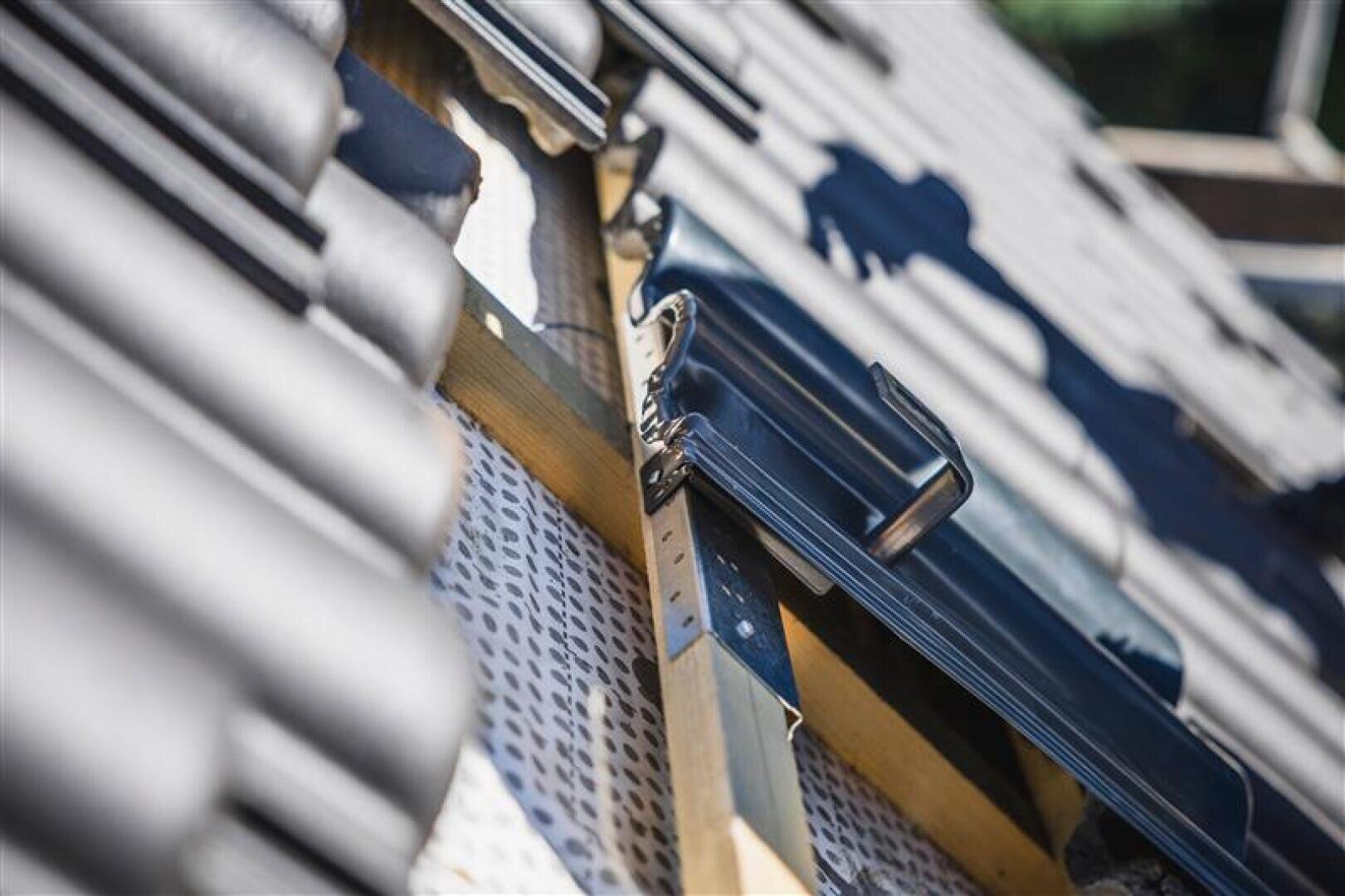 Nahaufnahme einer Dachkonstruktion mit schwarzen Dachziegeln, Holzlatten und Metallklammern, die die Verlegung von Dachmaterialien auf einem Schrägdach veranschaulichen.
