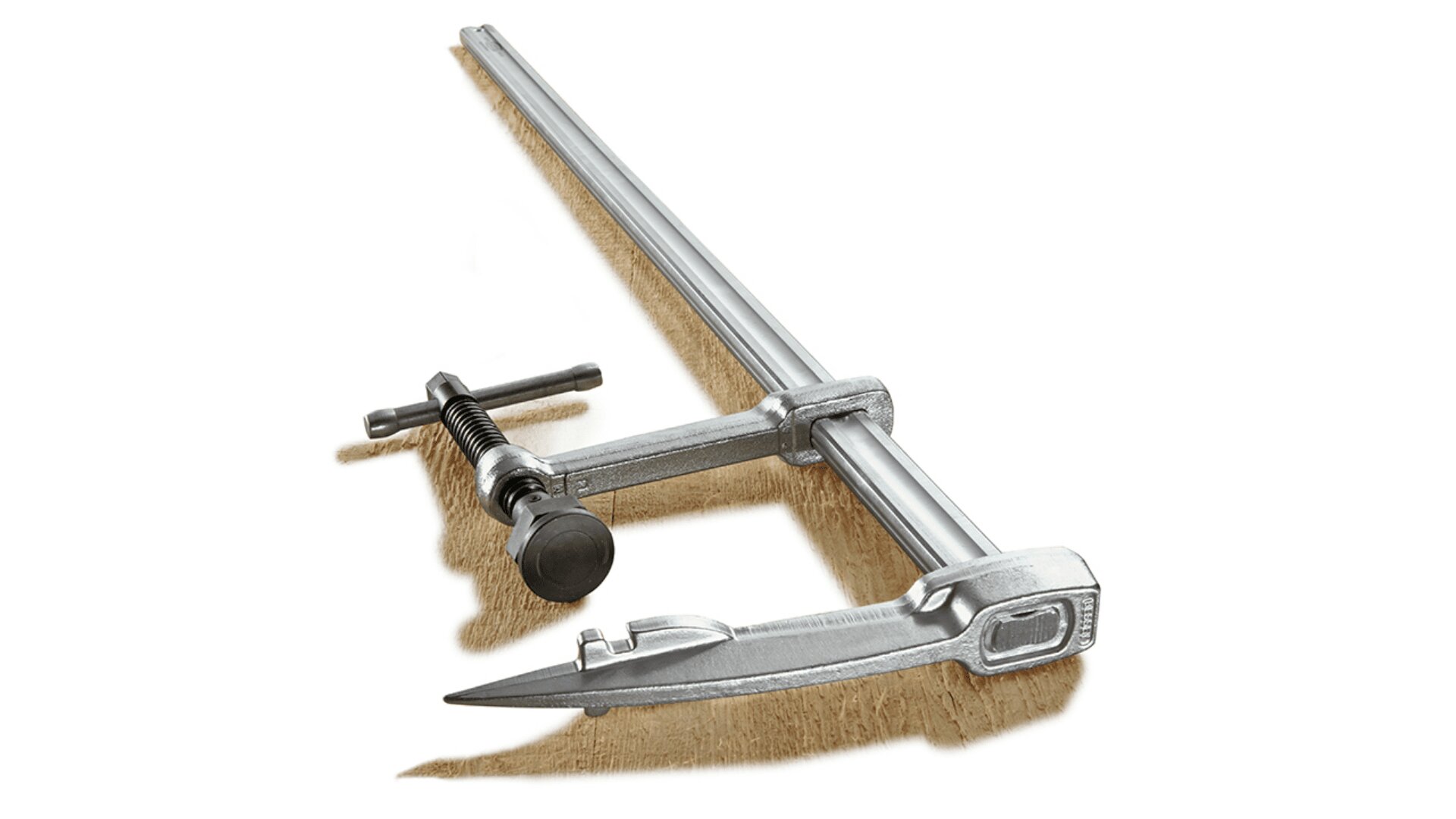 Eine Metall-Stangenklemme ist auf einem Stück Holz positioniert. Die Klemme ist silberfarben und verfügt über einen Gewindegriff zum Festziehen und Sichern von Objekten. Der Hintergrund ist schlicht weiß.