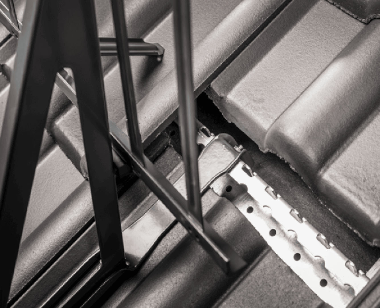 Close-up of a metal roof structure installed on gray roof tiles, showing the metal brackets and beams attached to the roof surface.