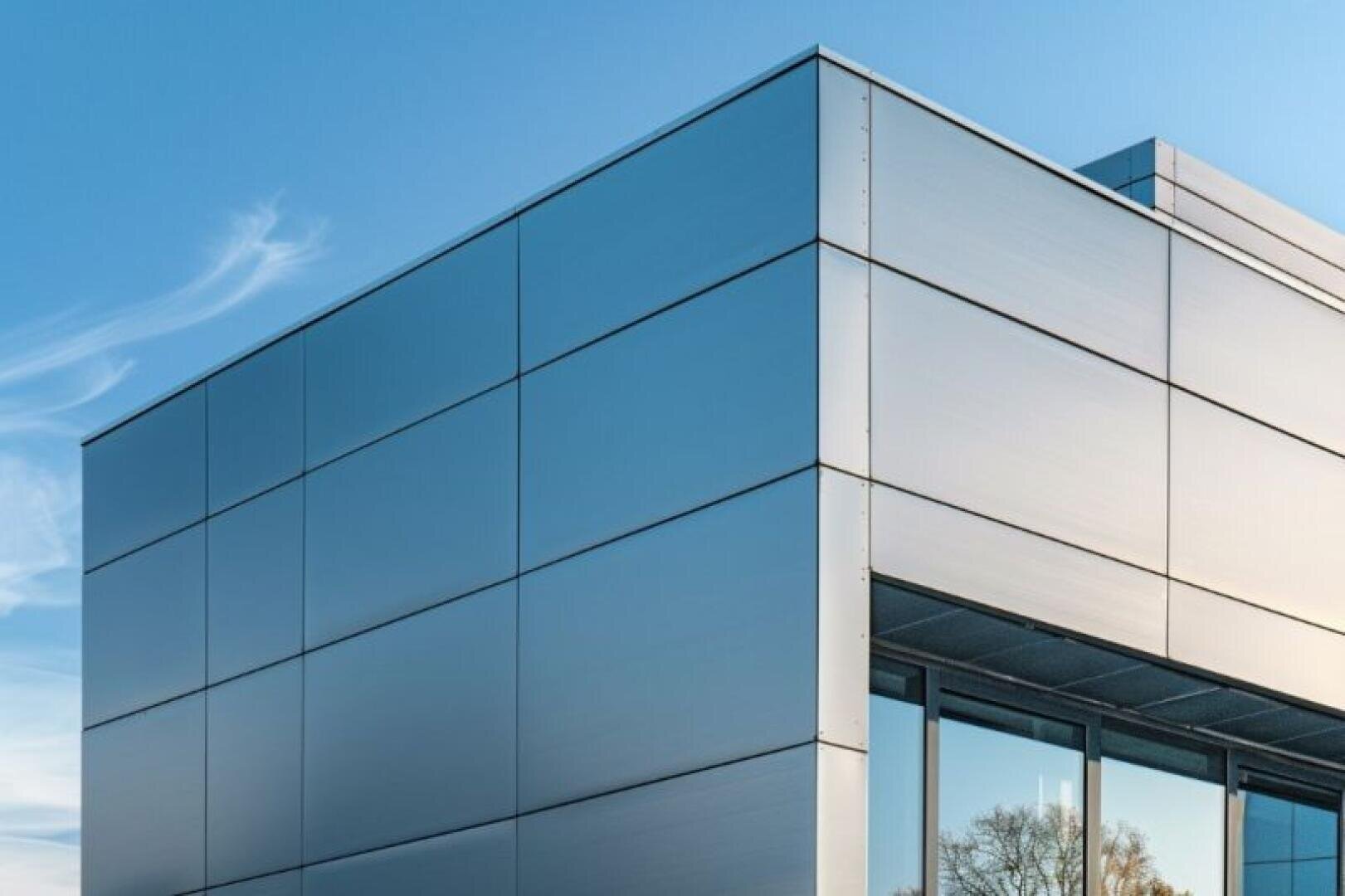 Modernes Gebäude mit glatter, metallischer Fassade und großen spiegelnden Fenstern vor einem klaren blauen Himmel mit Wolkenfetzen.