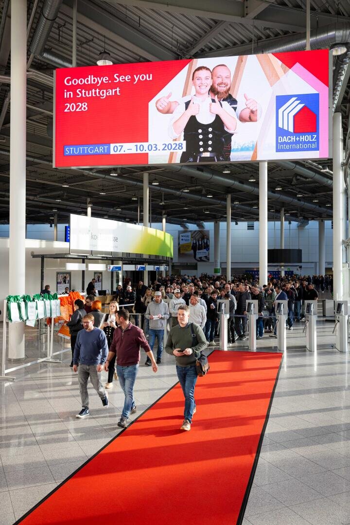 Eine Menschenmenge läuft über einen roten Teppich in einem Kongresszentrum. Über ihnen steht ein großes digitales Schild mit der Aufschrift "Auf Wiedersehen. Wir sehen uns in Stuttgart 2028" und wirbt damit für die Veranstaltung DACH+HOLZ International.