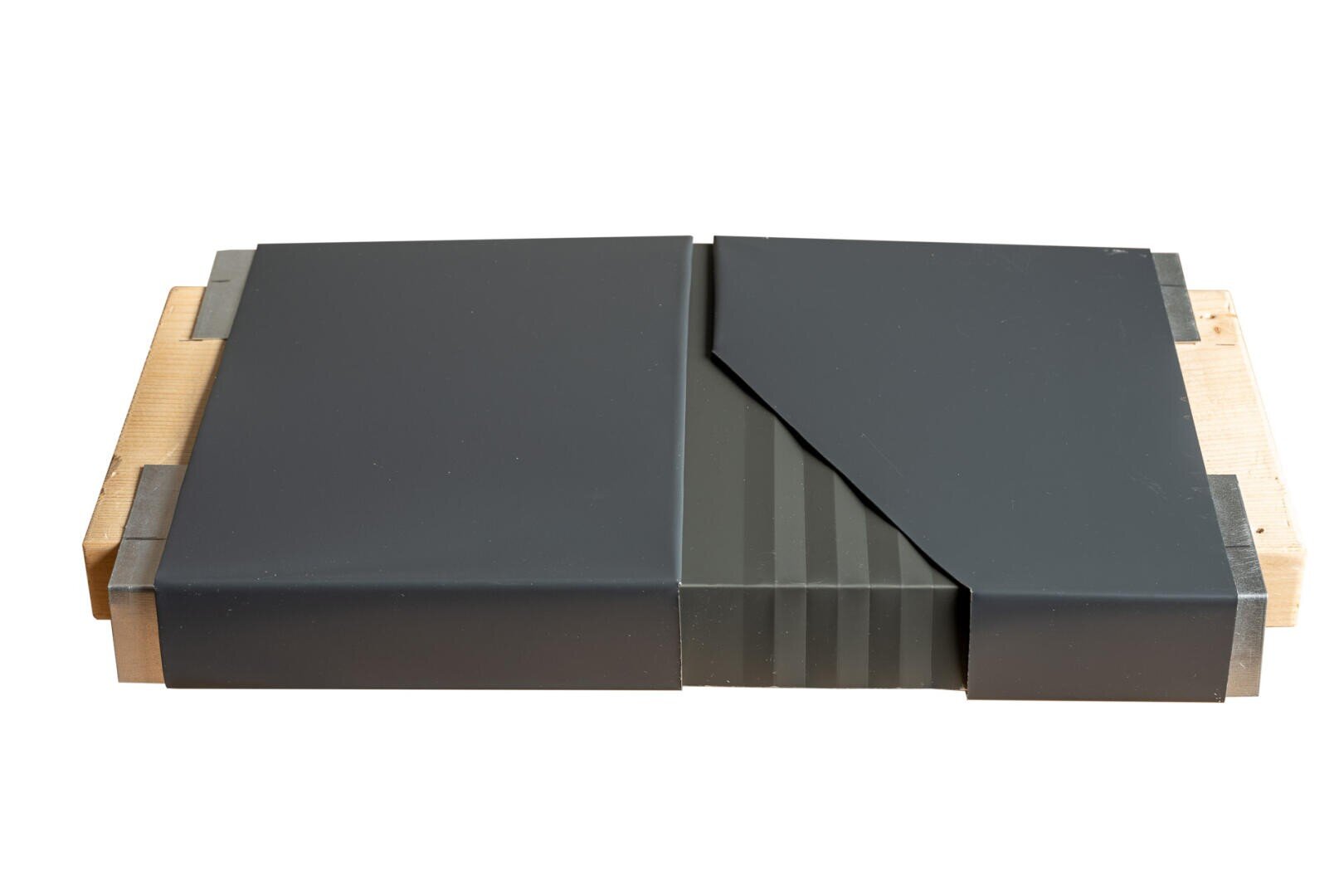 Ein rechteckiger Holzsockel trägt zwei schwarze rechteckige Platten, von denen eine teilweise von einem diagonal geschnittenen, sich überlappenden schwarzen Teil mit dezenten vertikalen Streifen bedeckt ist.