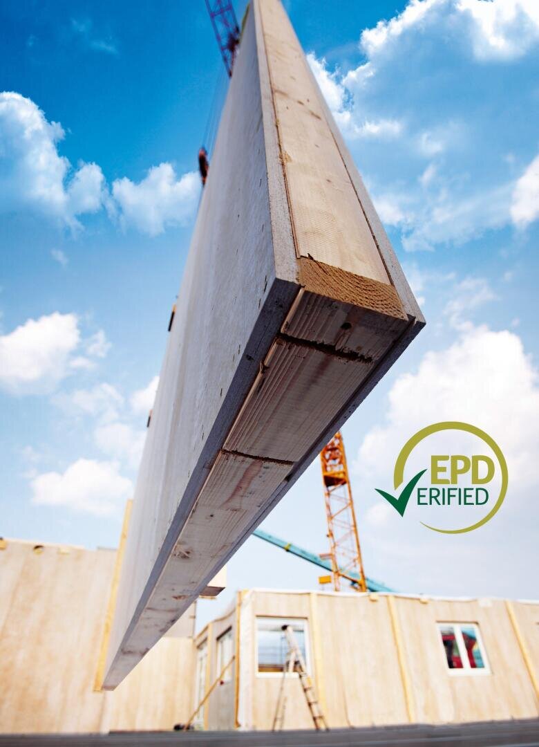Eine große vorgefertigte Holzwandplatte wird von einem Kran auf einer Baustelle hochgehoben. Der Himmel ist blau und wolkenverhangen, und im Vordergrund erscheint das Logo EPD VERIFIED.