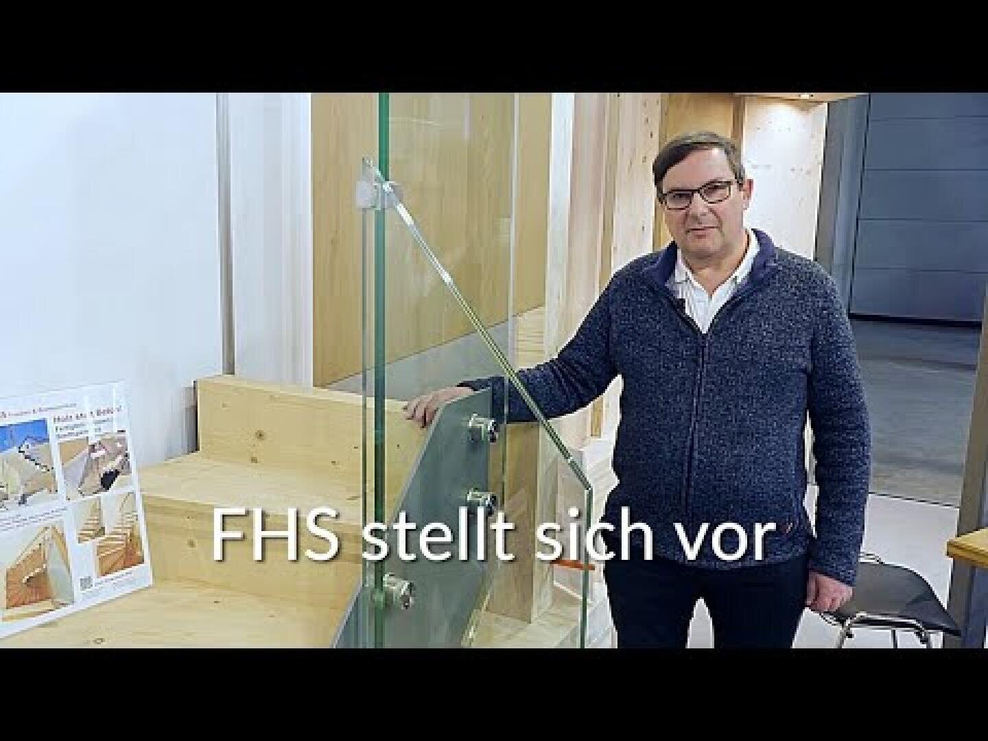 Ein Mann mit Brille und dunklem Pullover steht im Inneren neben einer Glaskonstruktion und einem Holzständer. Im Text auf dem Bild steht FHS stellt sich vor auf Deutsch.
