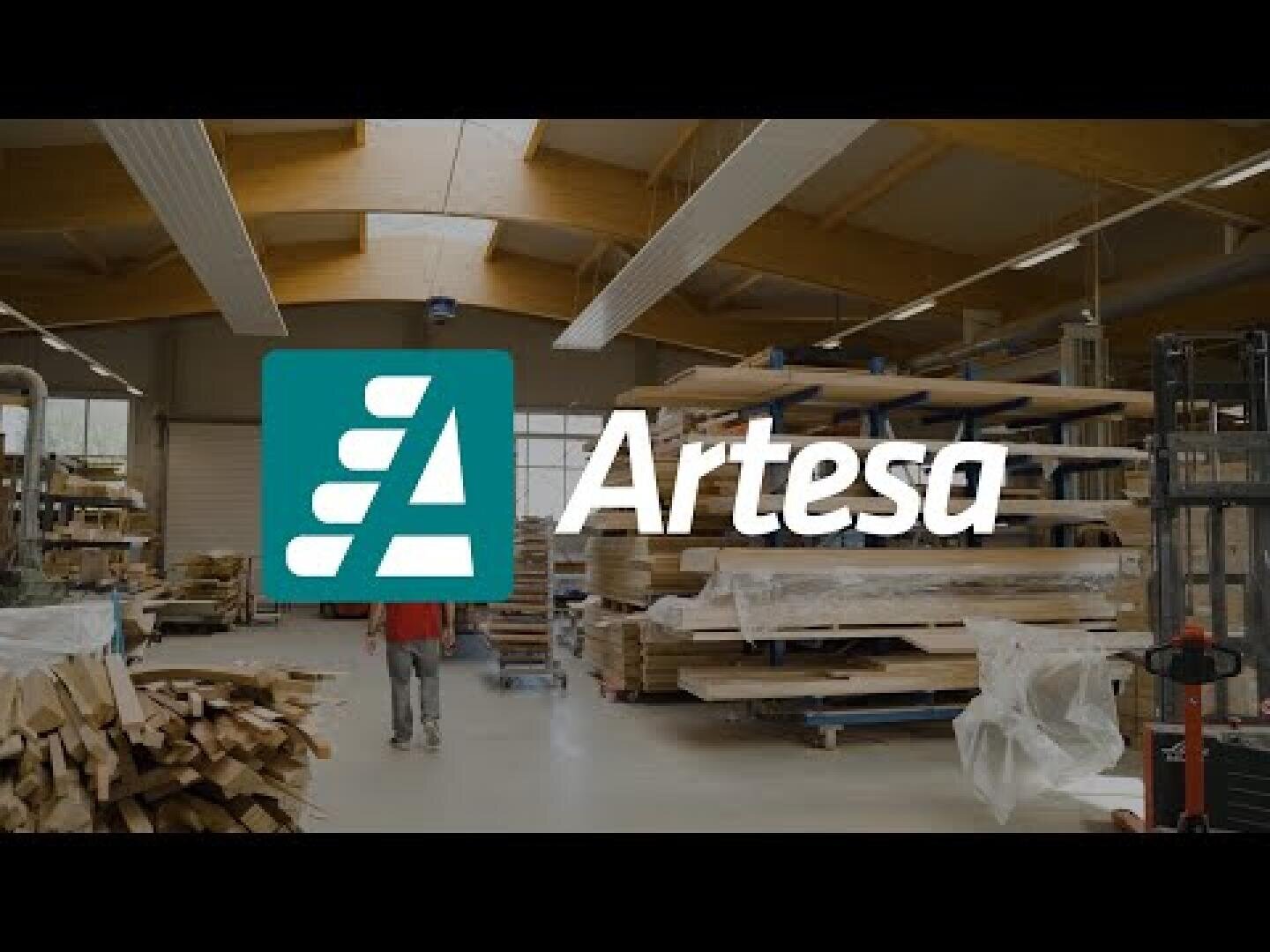 Eine geräumige Holzwerkstatt mit gestapeltem Holz und Maschinen; das Artesa-Logo und der Name sind in der Mitte des Bildes gut sichtbar angebracht.