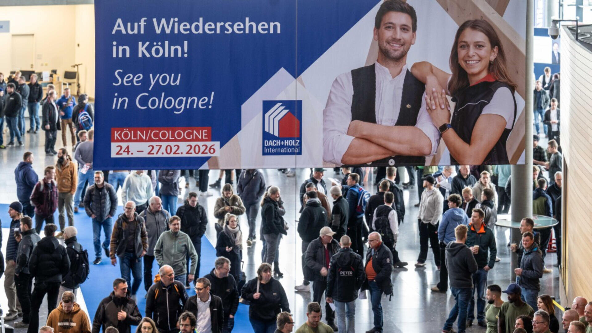 Eine große Menschenmenge betritt eine Veranstaltungshalle unter einem Banner mit zwei lächelnden Menschen und dem Text „Wir sehen uns in Köln! 24.–27.02.2026“ auf Englisch und Deutsch.