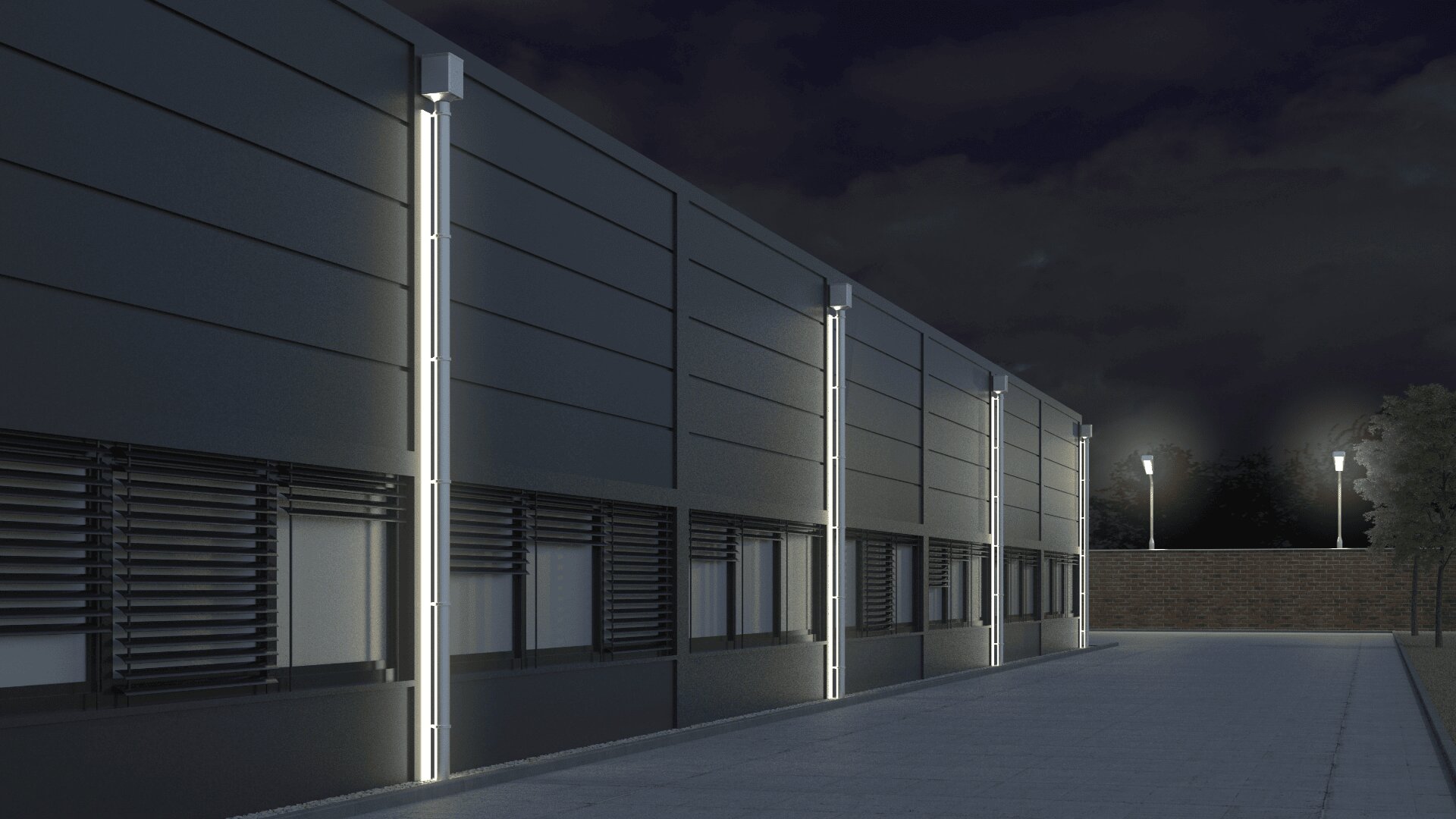 Ein modernes Gebäude bei Nacht mit vertikalen LED-Leuchten entlang der Wand, dunklen Fenstern mit Jalousien und einem gepflasterten Gehweg, der von Straßenlaternen gesäumt ist. Im Hintergrund sind Bäume und eine Ziegelmauer bei bewölktem Himmel zu sehen.