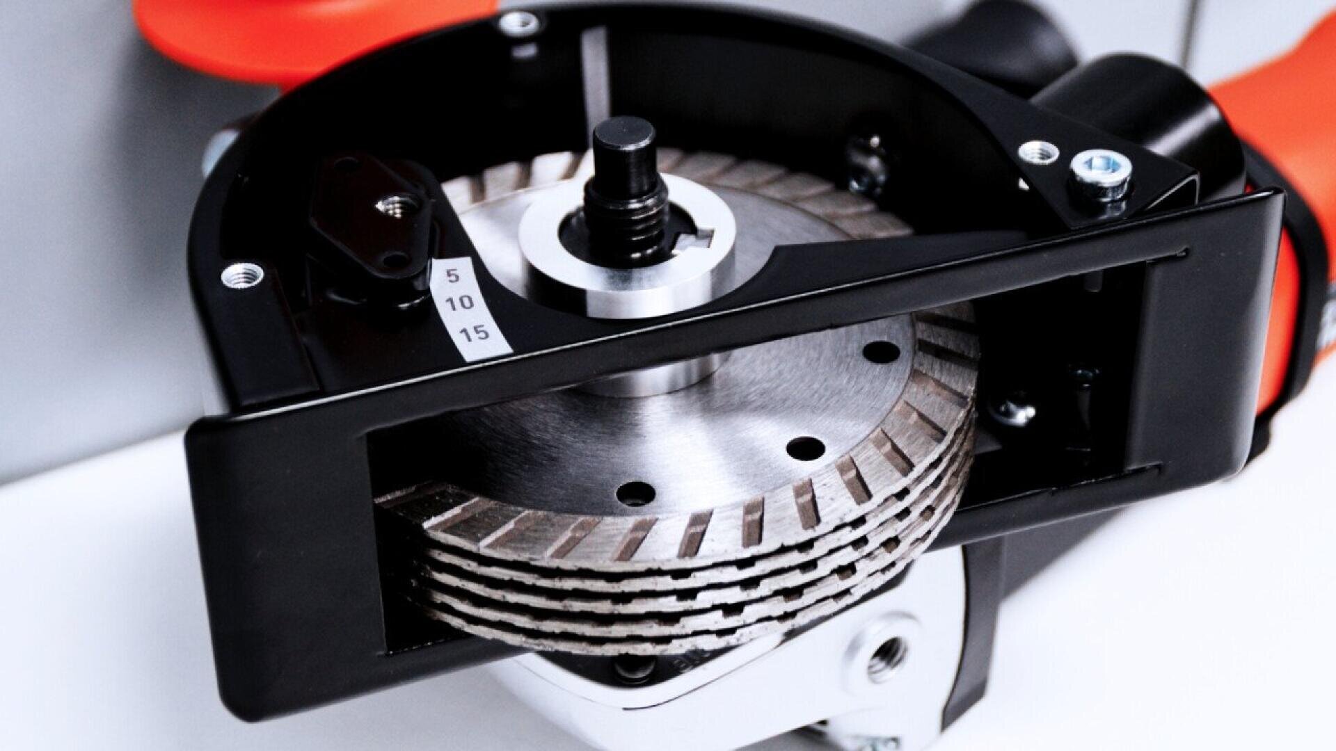 Close-up view of a stack of segmented circular saw blades mounted in a black and orange power tool, with a numbered adjustment gauge visible on the side.