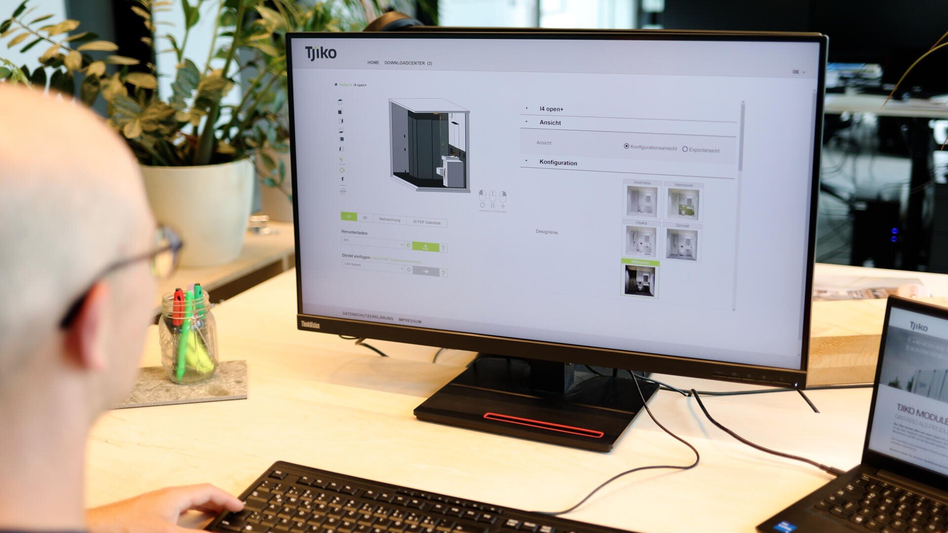 Eine Person verwendet einen Desktop-Computer, um auf der Tjiko-Website ein 3D-Raumkonfigurationstool anzuzeigen, bei dem verschiedene Anpassungsoptionen und Bilder auf dem Bildschirm angezeigt werden.