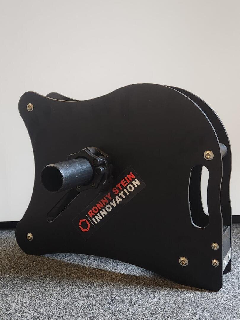 Eine schwarze, gitarrenförmige Spule mit einem Griff und der Aufschrift RONNY STEIN INNOVATION steht aufrecht auf einem grauen Teppich vor einer schlichten weißen Wand.