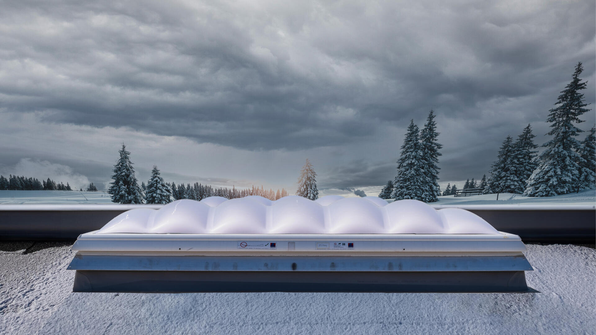 Ein großes, weißes, kuppelförmiges Dachfenster befindet sich auf einem verschneiten Dach mit schneebedeckten Bäumen und einem bewölkten Himmel im Hintergrund.