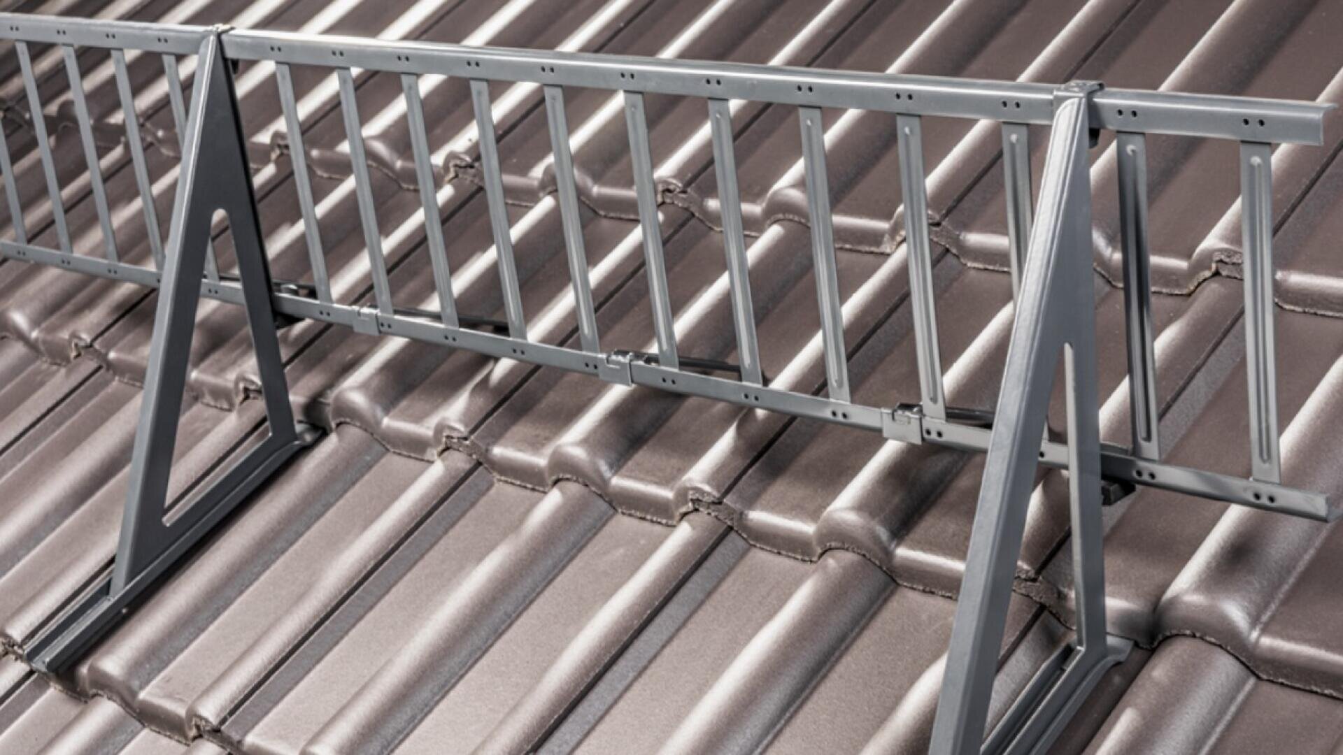 A metal snow guard is installed on a brown, tiled pitched roof to prevent snow from sliding off.