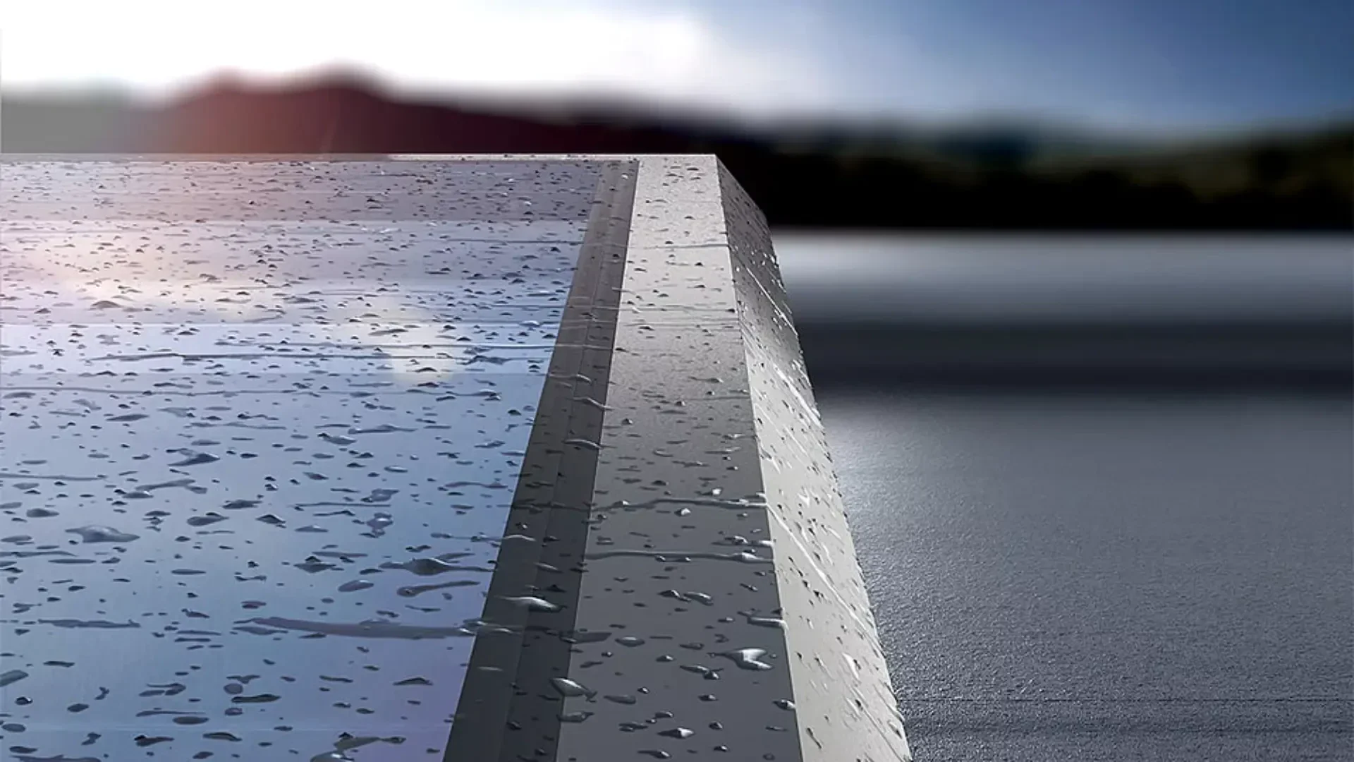 Eine Nahaufnahme einer glatten, reflektierenden Oberfläche, möglicherweise Metall oder Glas, mit Wassertropfen darauf. Der Hintergrund ist unscharf und zeigt eine Außenszene mit Wasser und Bergen unter einem bewölkten Himmel.