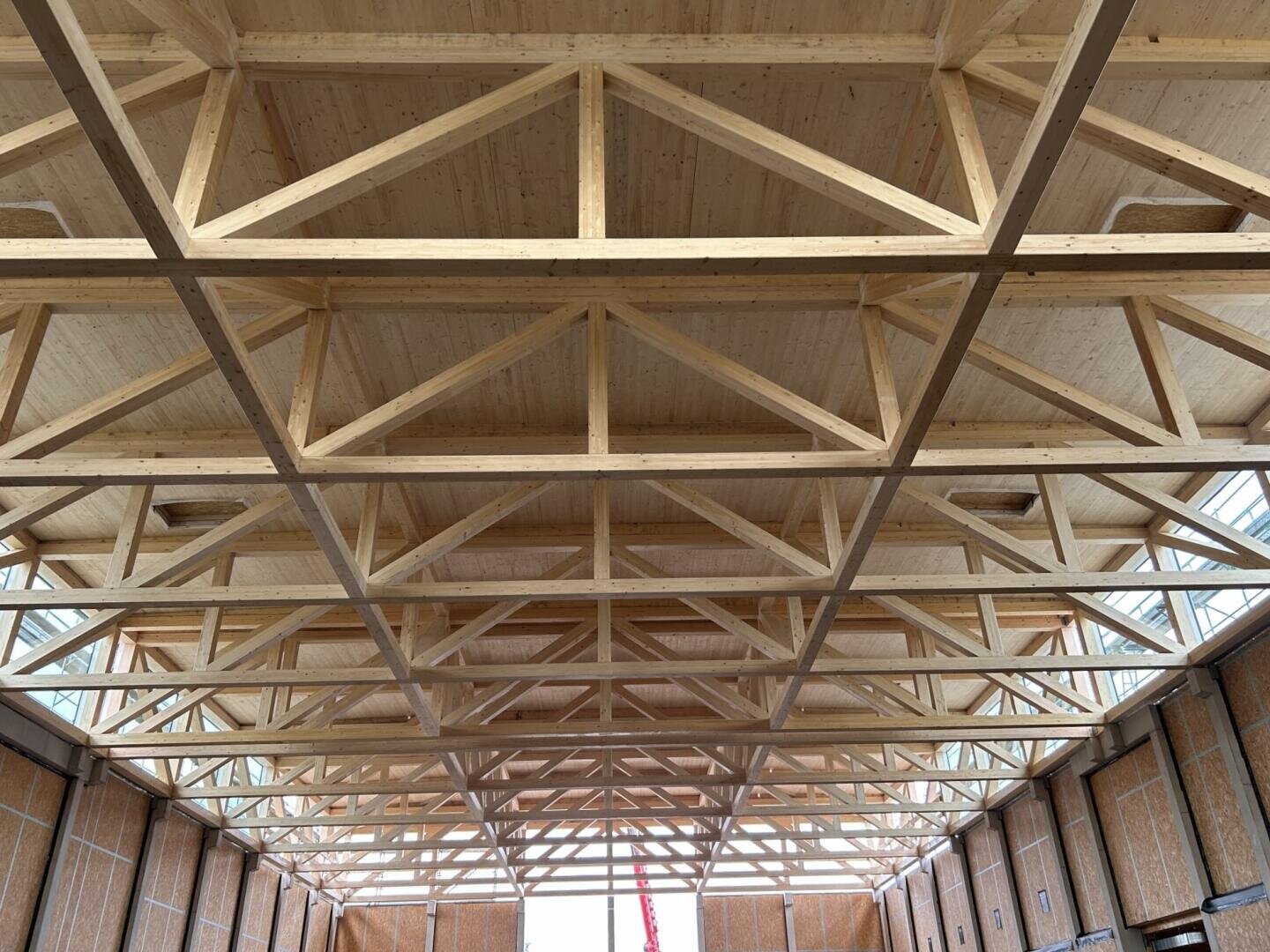 Hölzerne Dachstühle mit einem dreieckigen Muster stützen die Decke eines großen, unvollendeten Gebäudes. Durch die Fenster an den oberen Wänden fällt natürliches Licht ein und erhellt das Gebäude.