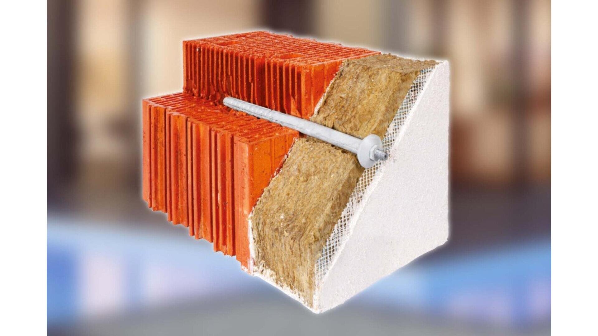 A cross-section of an insulated wall shows red bricks, a layer of yellow insulation, and an outer white coating, with a long metal fastener penetrating through all layers. The background is blurred.