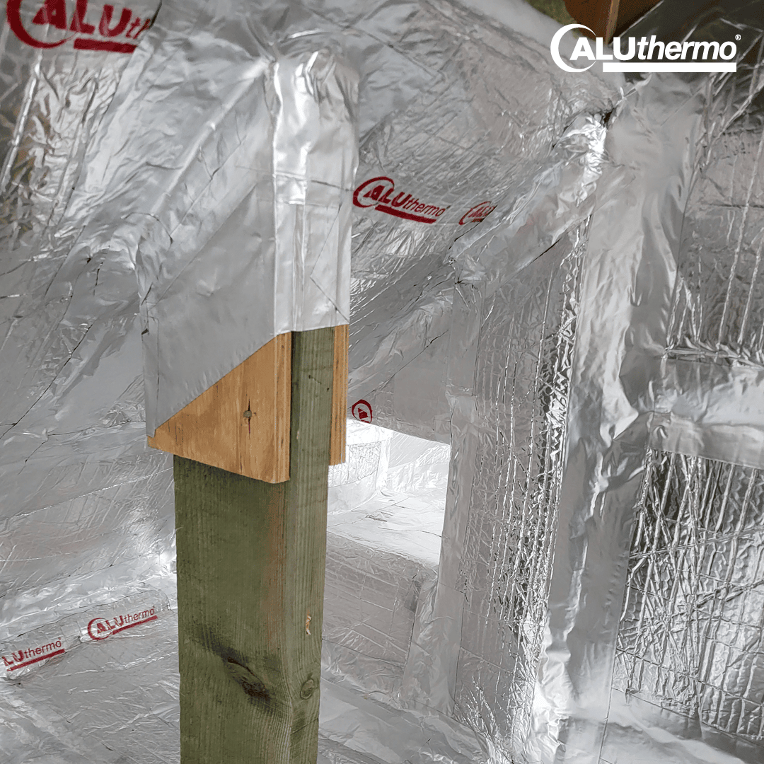 A wooden beam supports a structure clad in shiny metallic insulating material with the inscription "ALUthermo". The reflective surface covers the walls and ceiling.