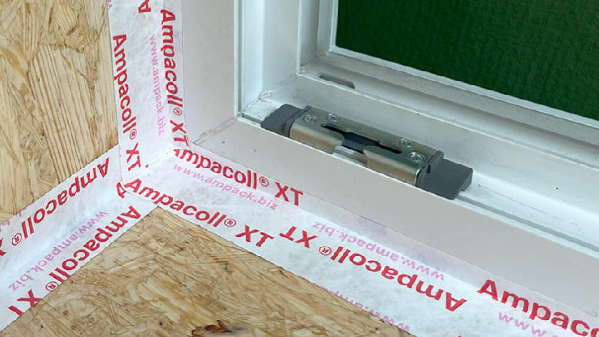 Close-up of a window frame being sealed with Ampacoll XT tape; the tape is applied neatly around the white frame and adjoining timber surfaces to ensure airtightness and insulation.