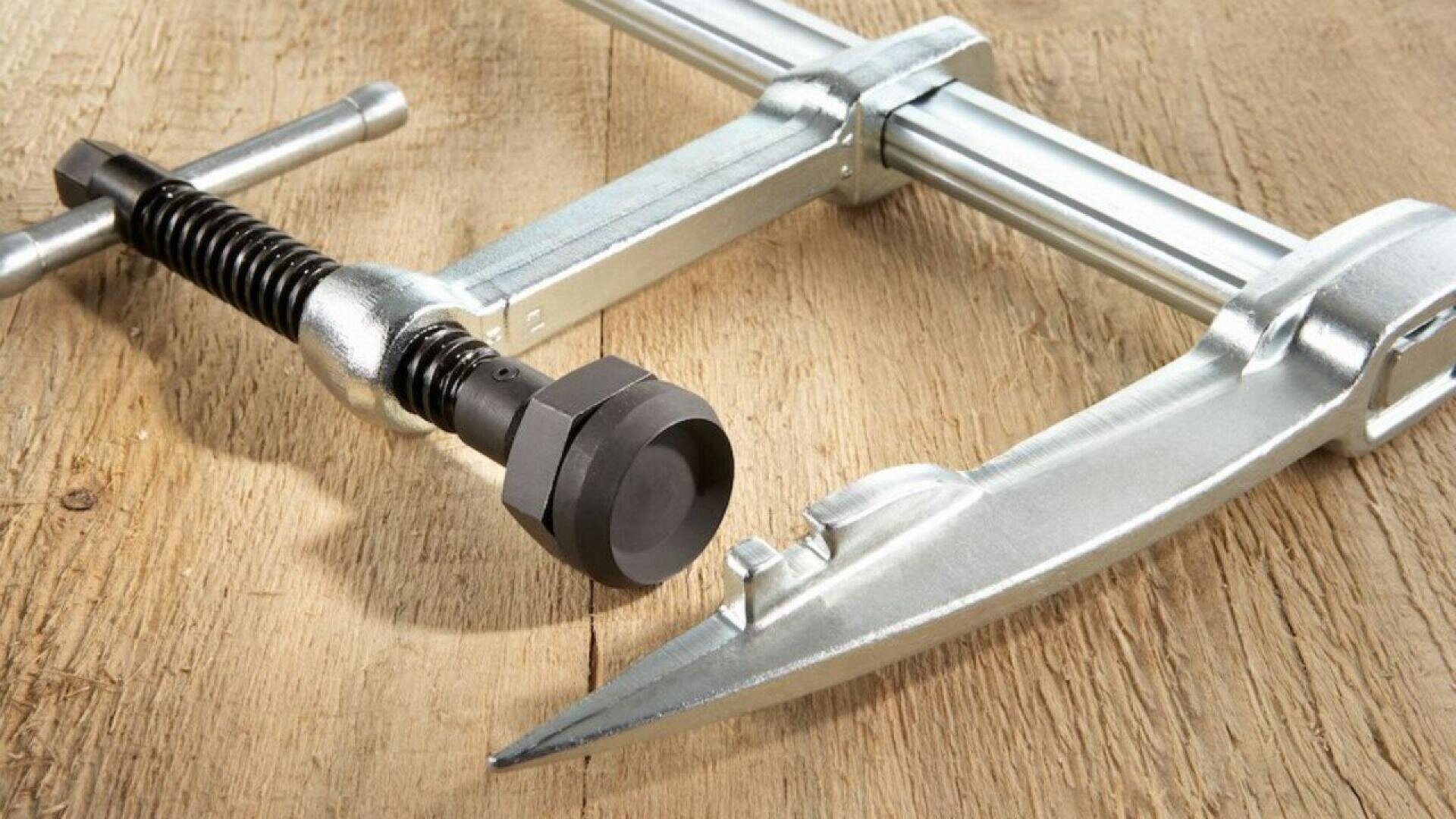 A close-up of a metal puller tool resting on a wooden surface, showing its screw mechanism and pointed arms.