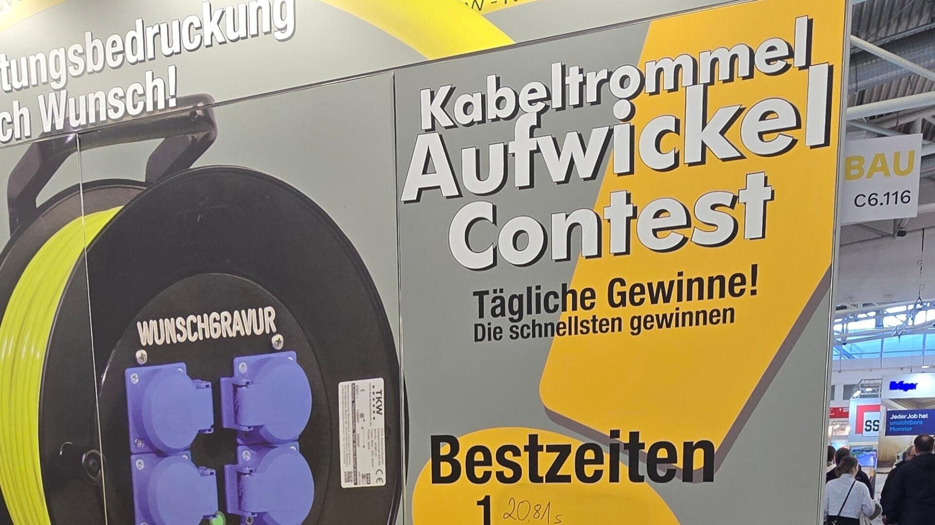 Ein gelb-schwarzes Schild an einem Veranstaltungsstand wirbt für einen Kabeltrommel-Aufwickel-Wettbewerb mit täglichen Preisen für die schnellsten Zeiten. Neben dem Schild ist eine Kabeltrommel mit Wunschgravur zu sehen.
