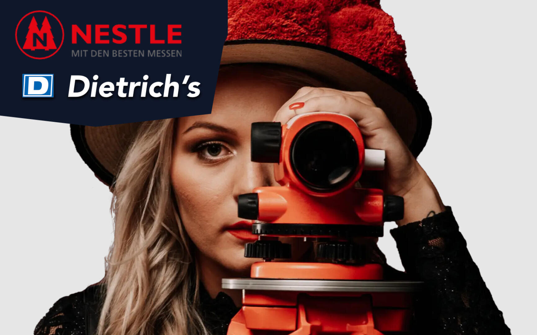 Eine Frau mit langen blonden Haaren blickt durch ein orangefarbenes Vermessungsinstrument und trägt einen roten, strukturierten Hut. In der oberen linken Ecke sind Logos für Nestle und Dietrich's mit deutschem Text zu sehen.