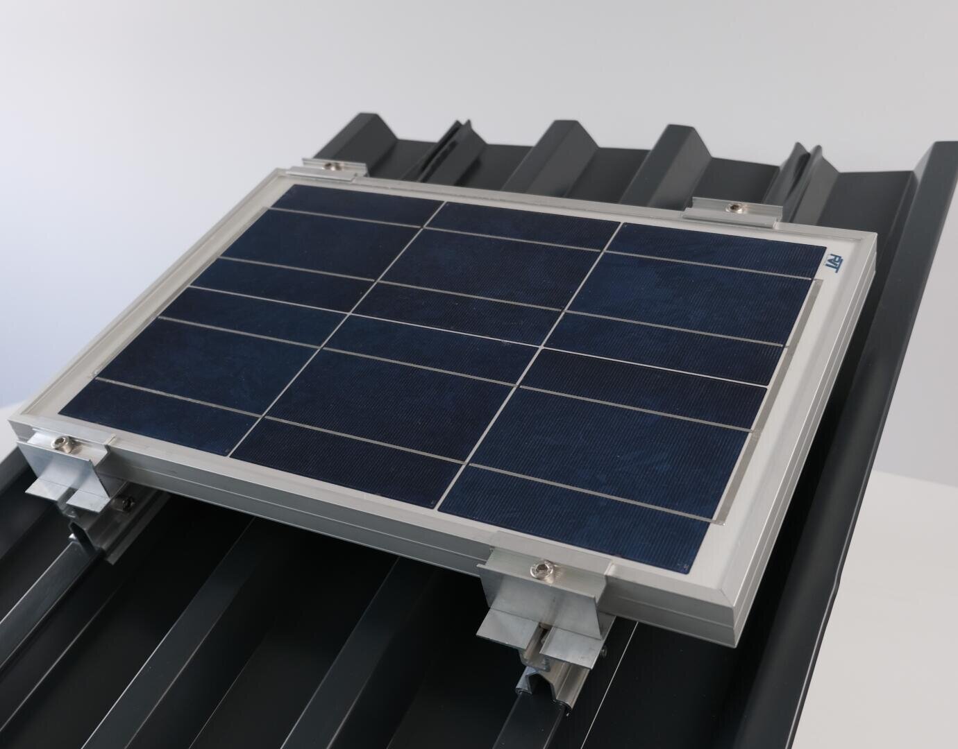 Ein kleines Solarmodul auf einem schwarzen Metalldach mit einem hellgrauen Rahmensystem, das in einem hellen Innenbereich gezeigt wird.