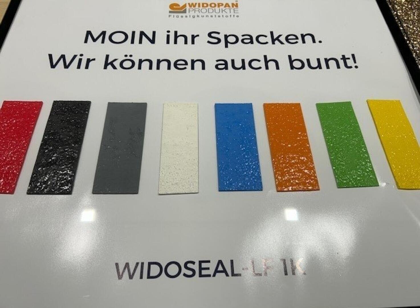 A display showing eight rectangular color samples—red, white, black, gray, blue, orange, green, and yellow—on a white background with German text and the brand name WIDOSEAL-LF 1K.