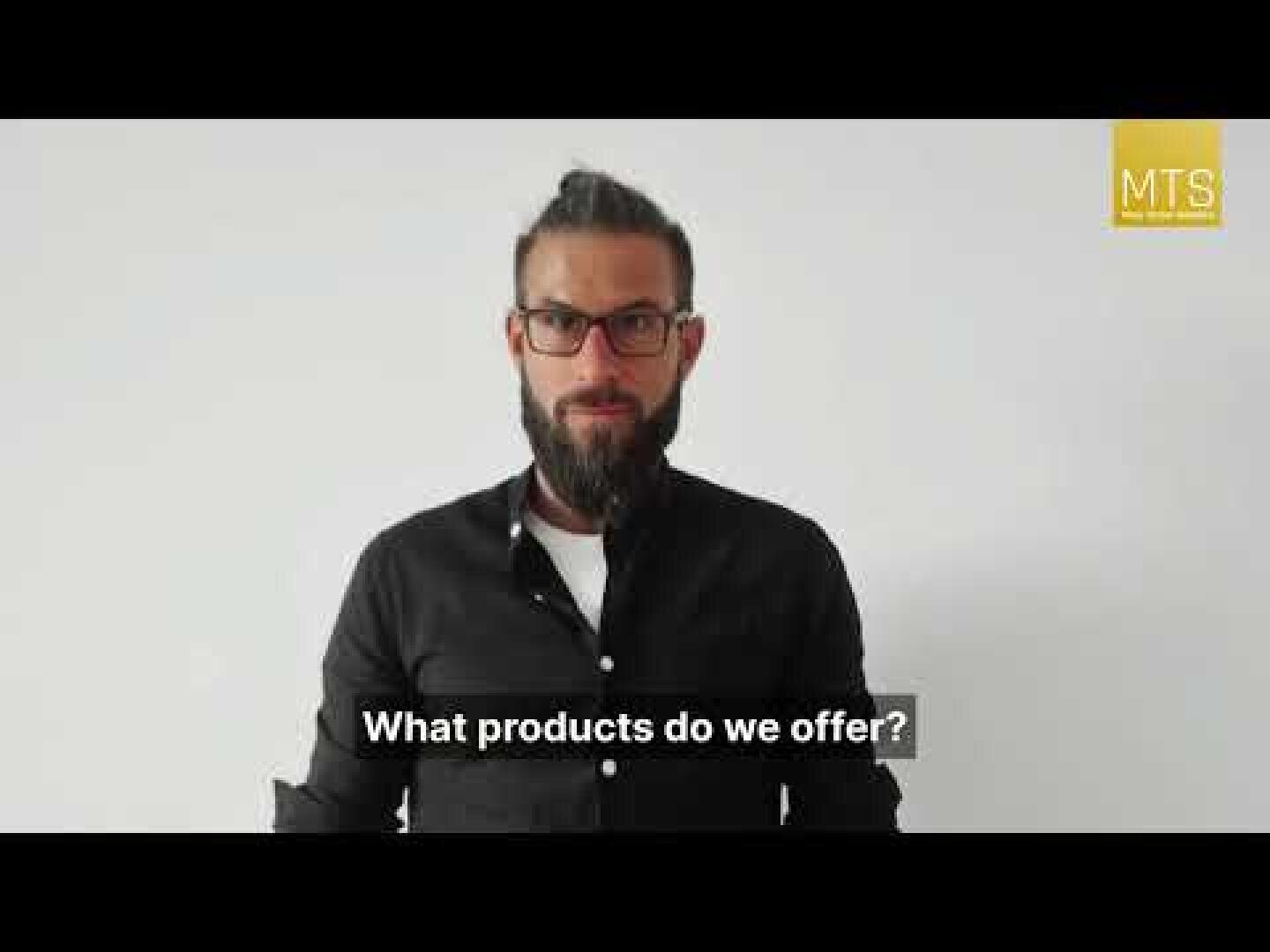 Ein Mann mit Brille und Bart steht vor einer schlichten weißen Wand und trägt ein schwarzes Hemd. Der überlagerte Text lautet: "Welche Produkte bieten wir an? In der oberen rechten Ecke erscheint ein gelbes MTS-Logo.