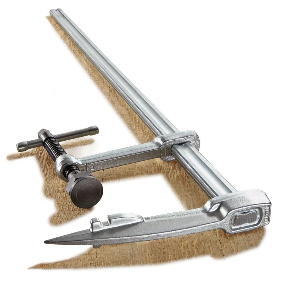 Ein Metallbügel mit einem Schraubgriff, der ein Stück Holz festhält und zum Zusammenhalten von Materialien bei der Holzbearbeitung oder bei Bauarbeiten verwendet wird.