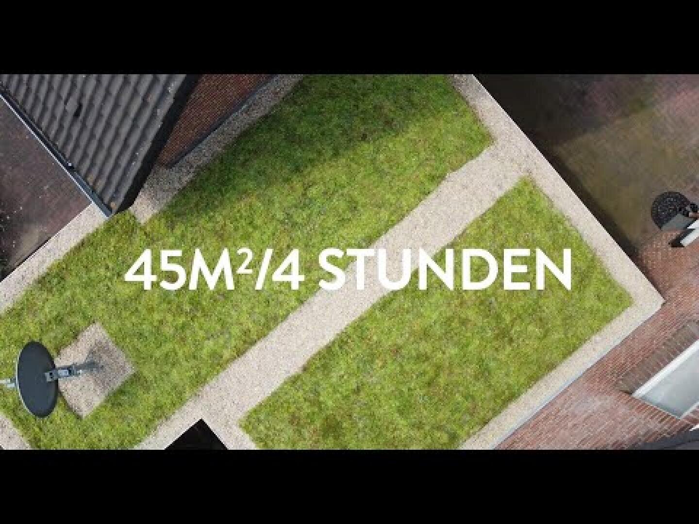 Aerial view of a rectangular lawn lined with gravel paths, on which the text 45M²/4 HOURS is superimposed in white letters. Parts of roofs and a satellite dish are visible.