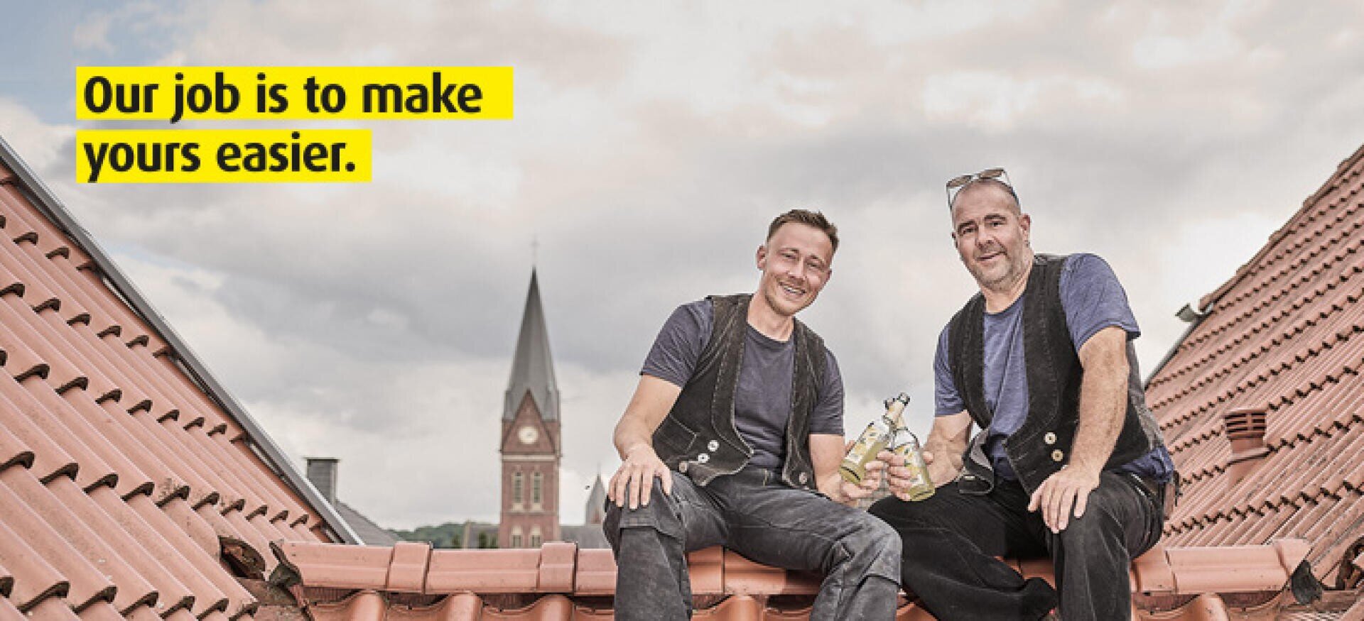 Two smiling workers in black vests sit on a tiled rooftop holding tools. In the background is a church steeple. Text on the image reads, Our job is to make yours easier.