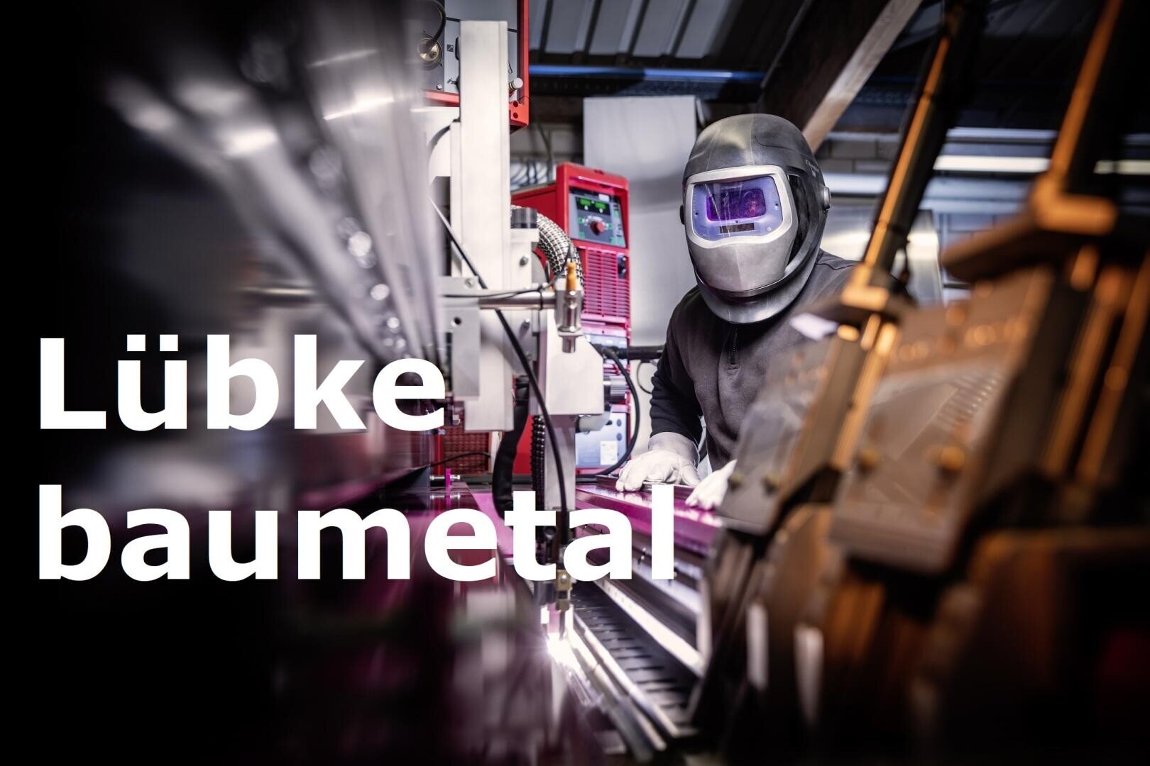 Eine Person, die einen Schweißerhelm trägt, arbeitet mit Metallgeräten in einer industriellen Umgebung. Der Text Lübke baumetal ist auf der linken Seite des Bildes eingeblendet.