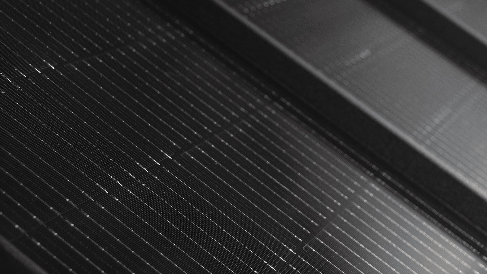 Nahaufnahme der Oberfläche eines Solarmoduls. Man sieht Reihen dunkler Photovoltaikzellen, die durch dünne weiße Linien getrennt sind, und den rechteckigen Rahmen des Moduls.