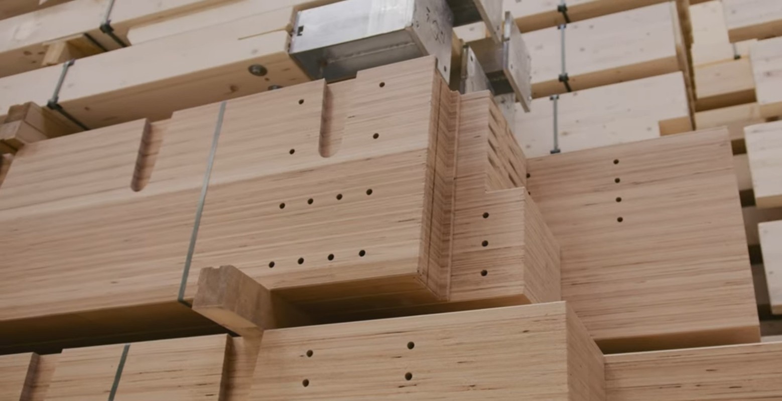 Stapel von zugeschnittenen Holzbalken mit zahlreichen Bohrungen und Nuten, die in einer Werkstatt oder einem Lagerhaus ordentlich angeordnet sind. Das Holz scheint f&uuml;r den Bau oder die Montage vorbereitet zu sein.