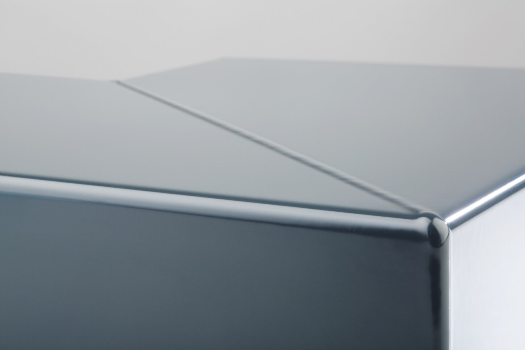 Eine Nahaufnahme einer glatten, metallischen Ecke mit glänzender Oberfläche, die eine diagonale Naht oder Falte aufweist, die quer über die Oberfläche verläuft.